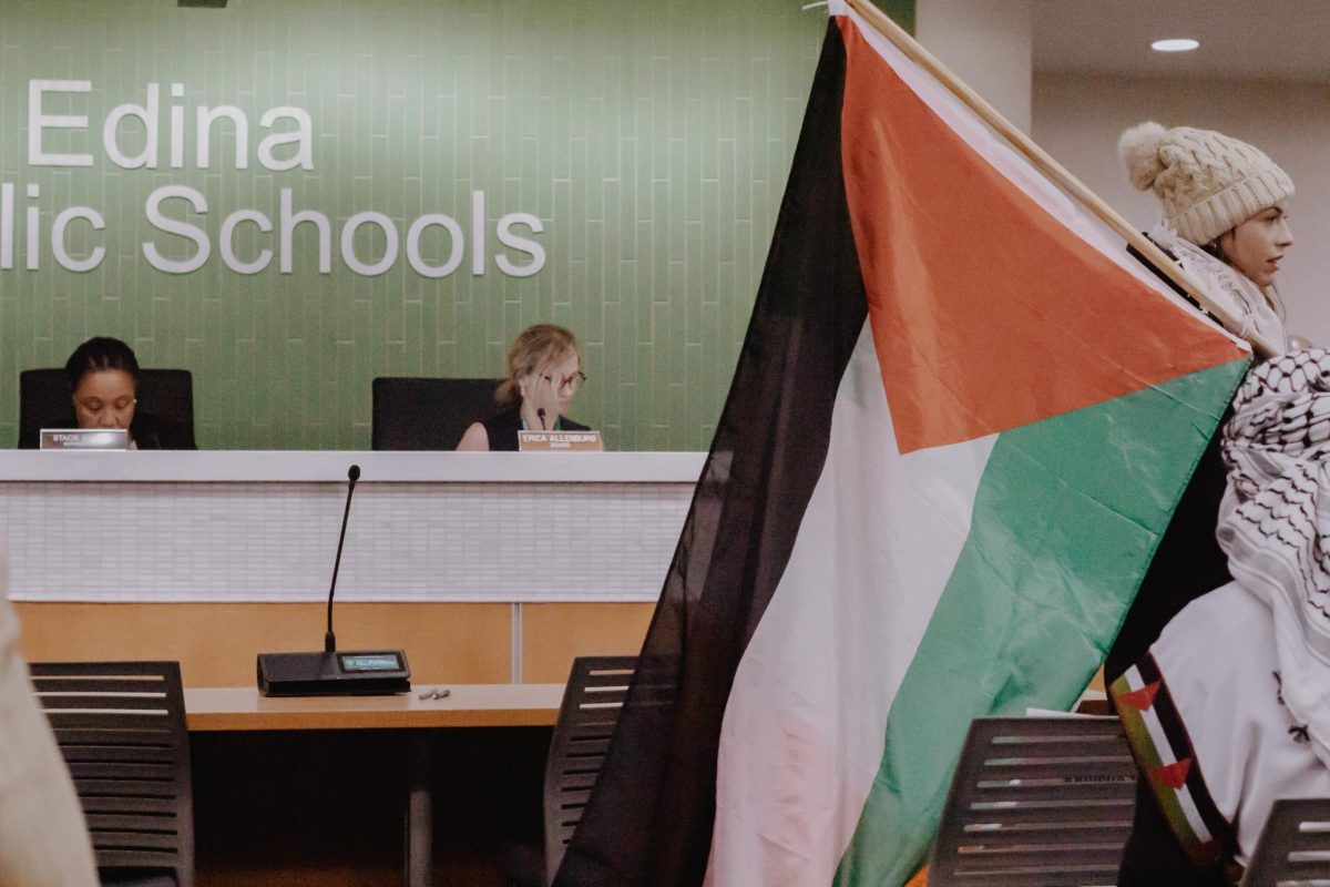 Woman carries Palestine flag while finding a seat before the School Board meeting.