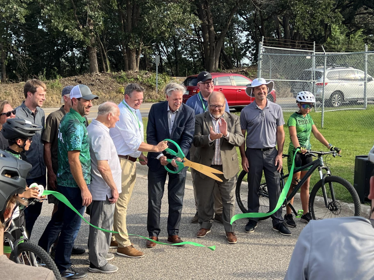 Edina mayor Jim Hovland cuts a ribbon celebrating new Braemar Park trails surrounded by City Parks & Recreation staff and Edina Mountain Biking coaches and students.